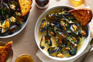 A bowl of moules mariniÃ¨res with a piece of bread in it.