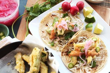 A platter of tacos with radishes, lime wedges and cilantro on the side.