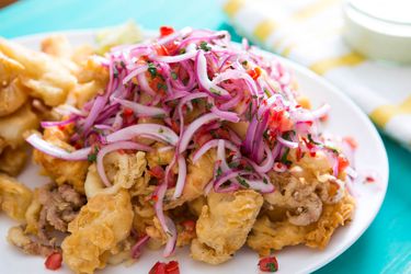 A pile of fried mixed seafood topped with lime-marinated red onions, tomatoes, and cilantro