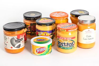 A group of nine queso dips in jars against a white background.