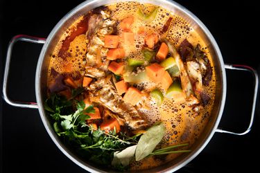 Overhead view of roasted turkey bones, browned vegetables, and herbs simmering in stockpot