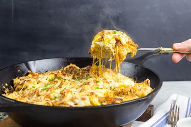 LIfting up a hefty spoonful of French onion strata out of a cast iron skillet