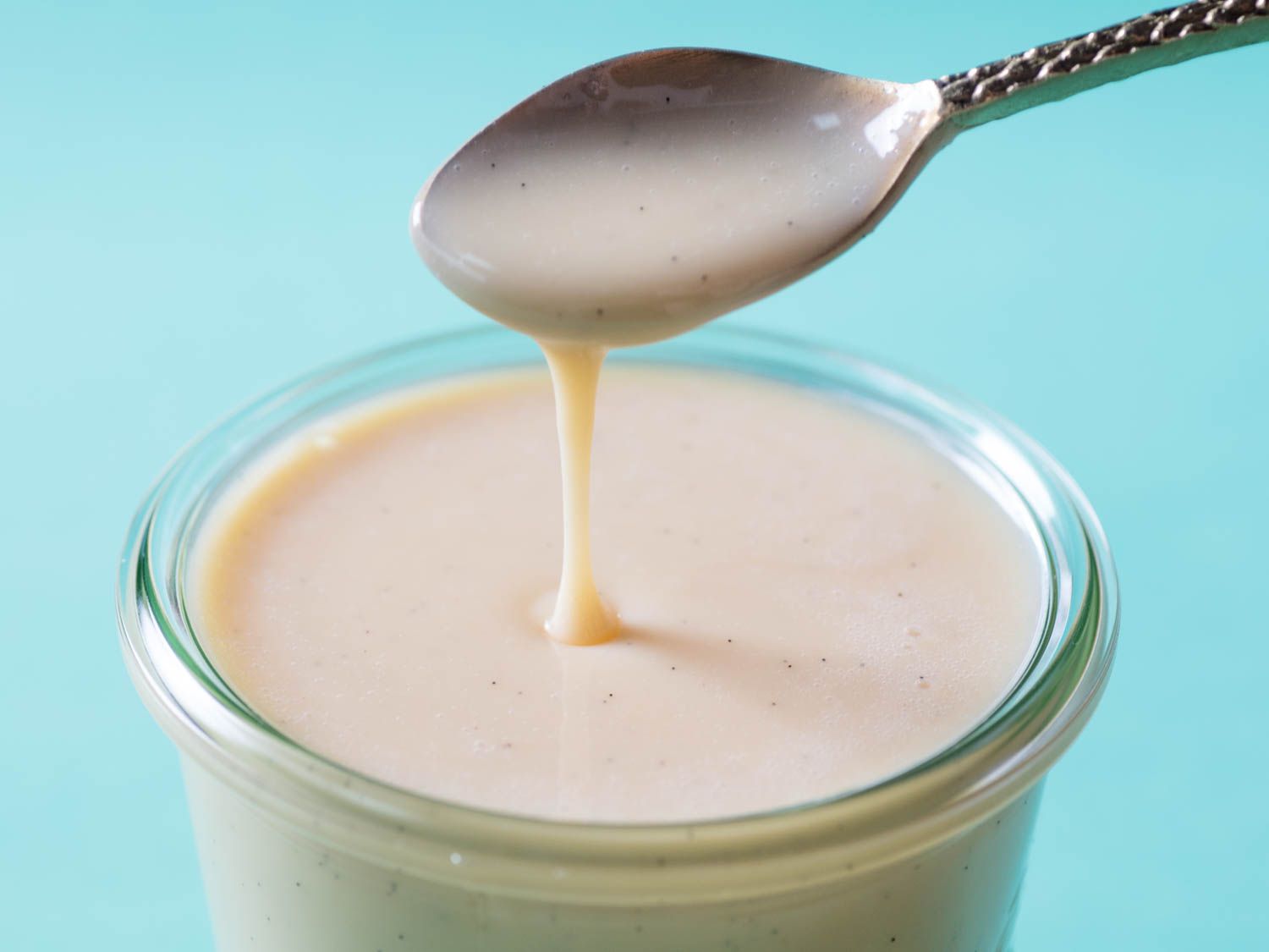 A spoon lifting out of a glass jar filled with homemade sweetened condensed milk.
