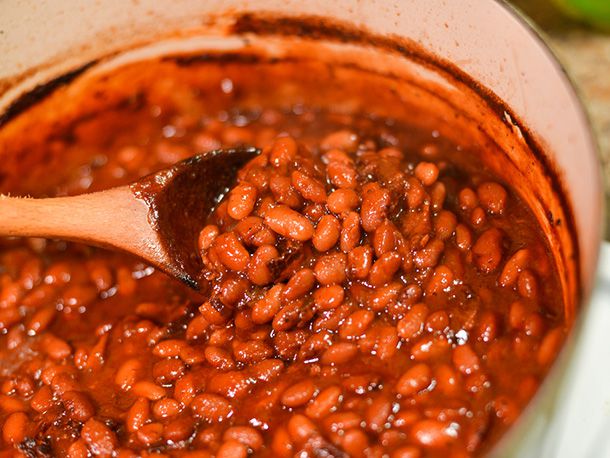 Barbecue baked beans being stirred with a wooden spoon in an enamel cast iron Dutch oven