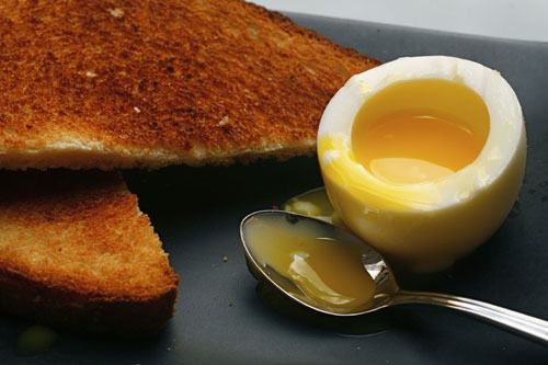 一个半熟的鸡蛋，切开后露出溏心蛋黄，旁边是一片吐司和一把勺子。gydF4y2Ba