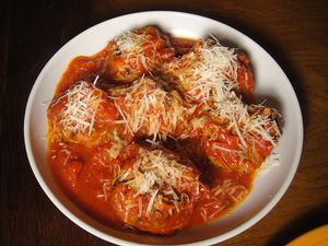 A plate of Frankie's meatballs in tomato sauce and topped with shredded cheese.