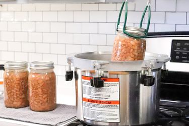 a jar of beans being lowered into an All-American brand pressure canner