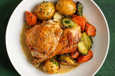 A white ceramic dish holding pan-roasted chicken and vegetables in jus.