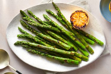 grilled asparagus served on a large serving plate, drizzled with olive oil, with lemon squeezed over the top, and garnished with charred lemons