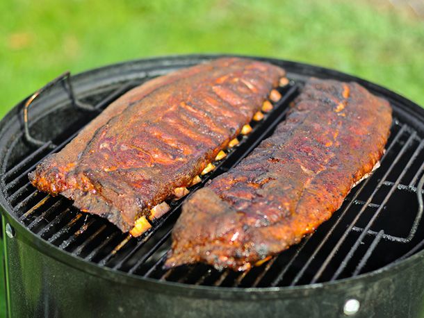 Two racks of barbecued pork spareribs sitting on the great of a smoker.