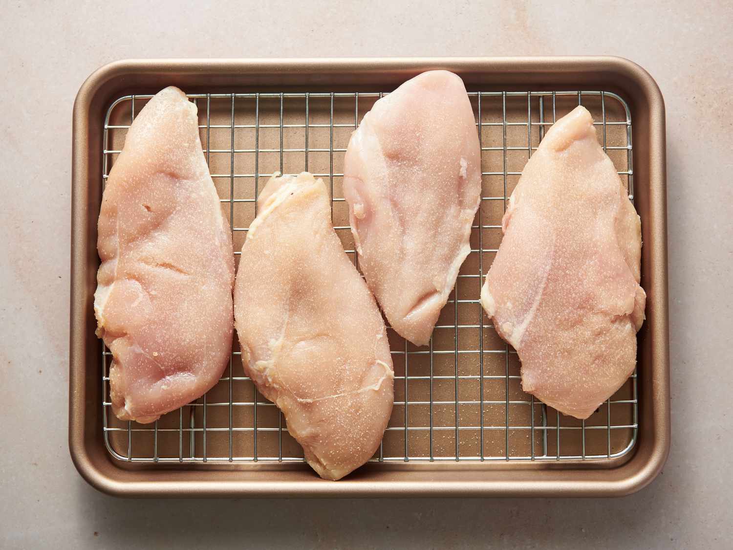 鸡胸肉慷慨地洒在两边用盐在一组线架边的烤盘gydF4y2Ba