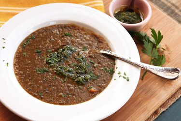 A big bowl of lentil soup, topped with gremolata, next to a small bowl of gremolata with olive oil for topping.