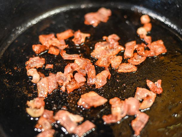 Chopped bacon rendering and browning in a cast iron skillet.