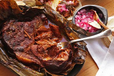 Cochinita Pibil wrapped in banana leaves with pickled diced red onion and tortillas.