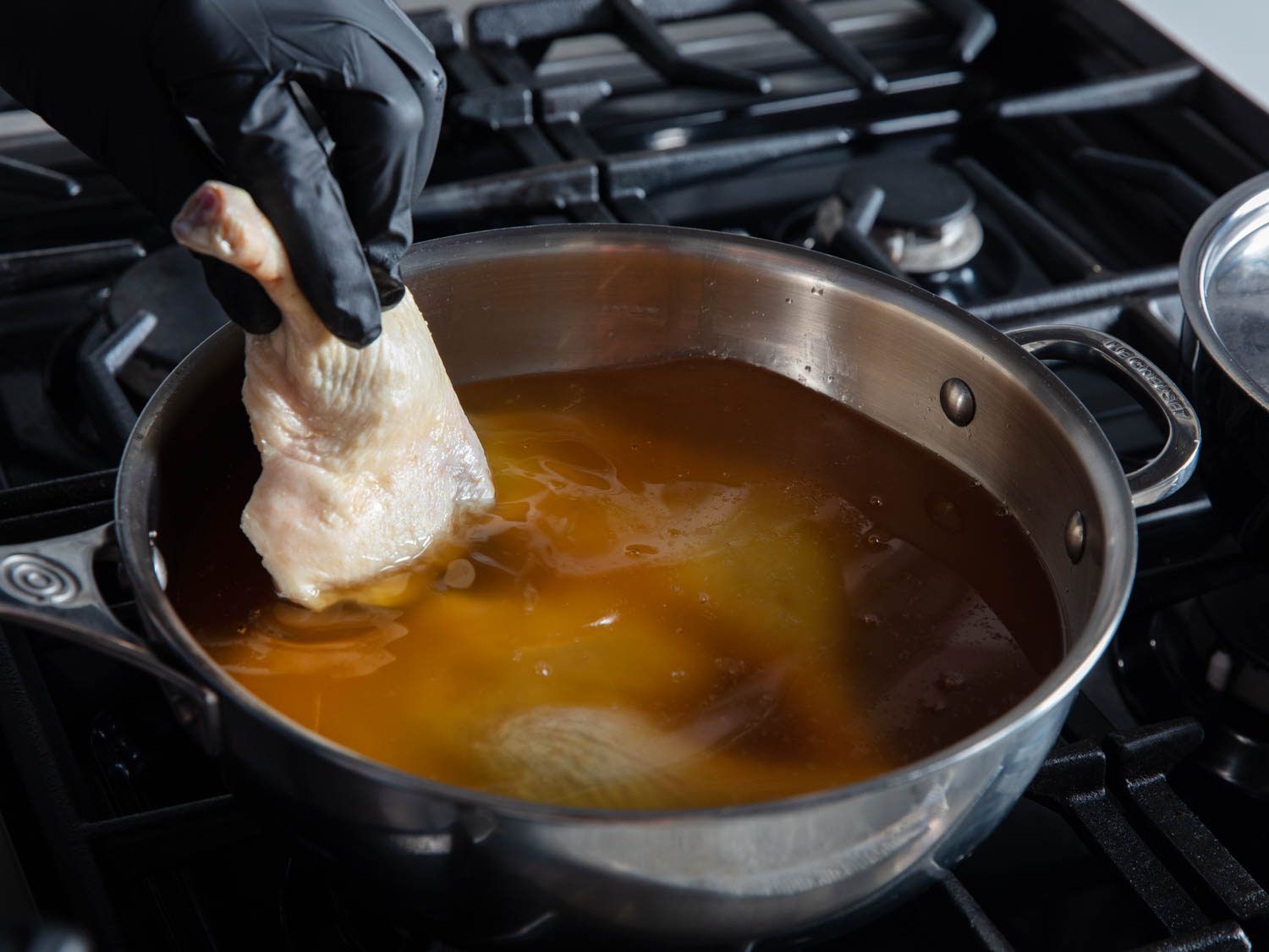 Lowering duck leg into saucepan of rendered fat.