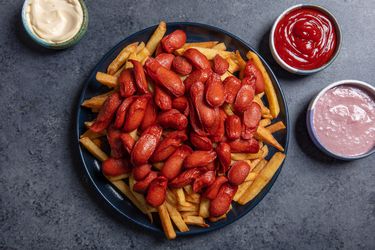 A large platter of salchipapa (french fries with sliced hot dogs piled on top) and a few dipping sauces alongside