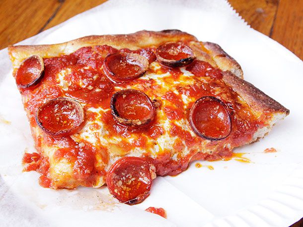 一块王子街的意大利辣香肠披萨，放在纸巾和白纸盘上;意大利辣香肠的边缘是卷曲的，略带棕色。