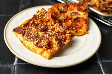 两块方形的西西里辣香肠披萨放在奶油色的瓷盘上。