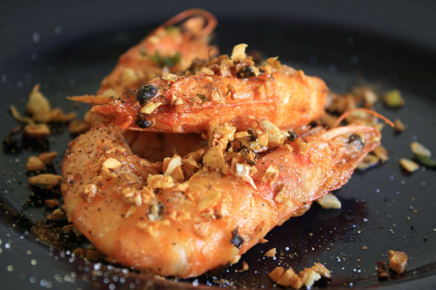这是两只中式油炸咸虾的特写，上面裹着棕色的大蒜、葱花和胡椒片。