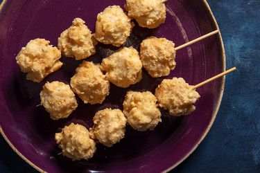 Three wood skewers with 4 squid balls each on a purple plate set against a blue background