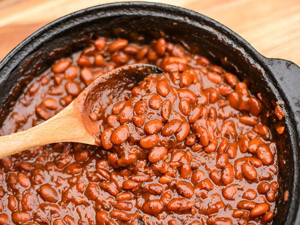 A crock of barbecue beans being stirred with a wooden spoon.