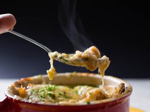 用勺子从红碗里舀出一口芝士法式洋葱汤。