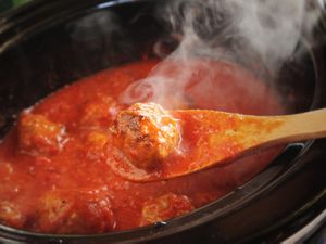slow cooker meat lifted out of tomato sauce with a wooden spoon