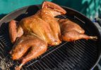 A spatchcocked turkey cooking on a grill.
