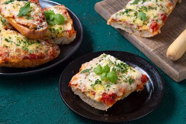 French bread pizza cut up and displayed on two ceramic plates and on a wooden cutting board.