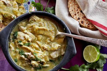 Bowl of pressure cooker green chili chicken (chile verde) with tortillas, cilantro, and limes