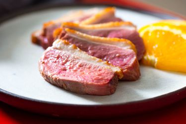 Medium-rare duck breast sliced and served on a plate with orange wedges