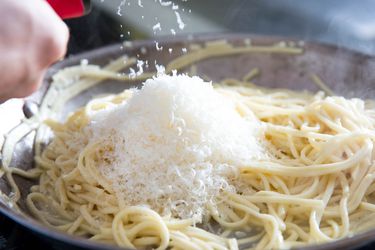 Showering grated cheese down into a skillet full of spaghetti