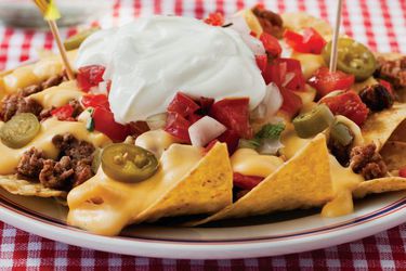 Homemade ball park nachos on a plate with sour cream on top.
