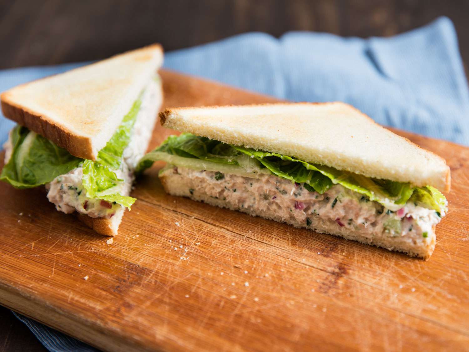 A tuna sandwich on a cutting board. The sandwich is cut in half on the diagonal and the cut side of one half is faced to the camera.