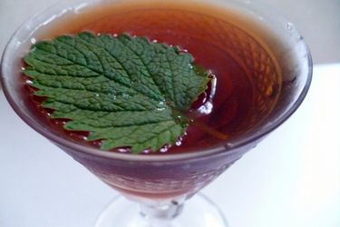 A cocktail glass with a cocktail garnished with a shiso leaf.