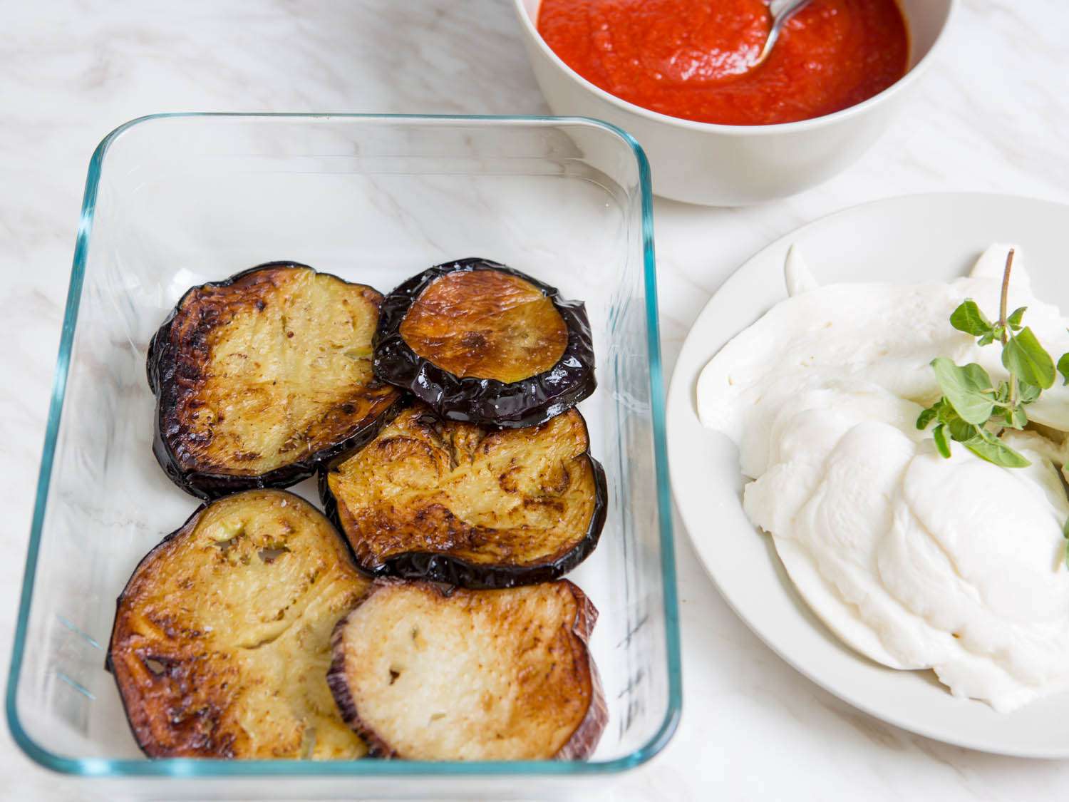 把炸茄子片和新鲜的马苏里拉奶酪分层放在烤盘中。