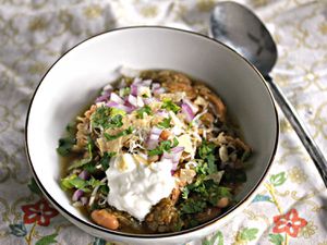 bowl of slow-cooker turkey chili verde topped with sour cream, herbs, and chopped red onion