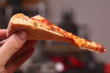 一只手拿着一片homemade New York-style cheese pizza.