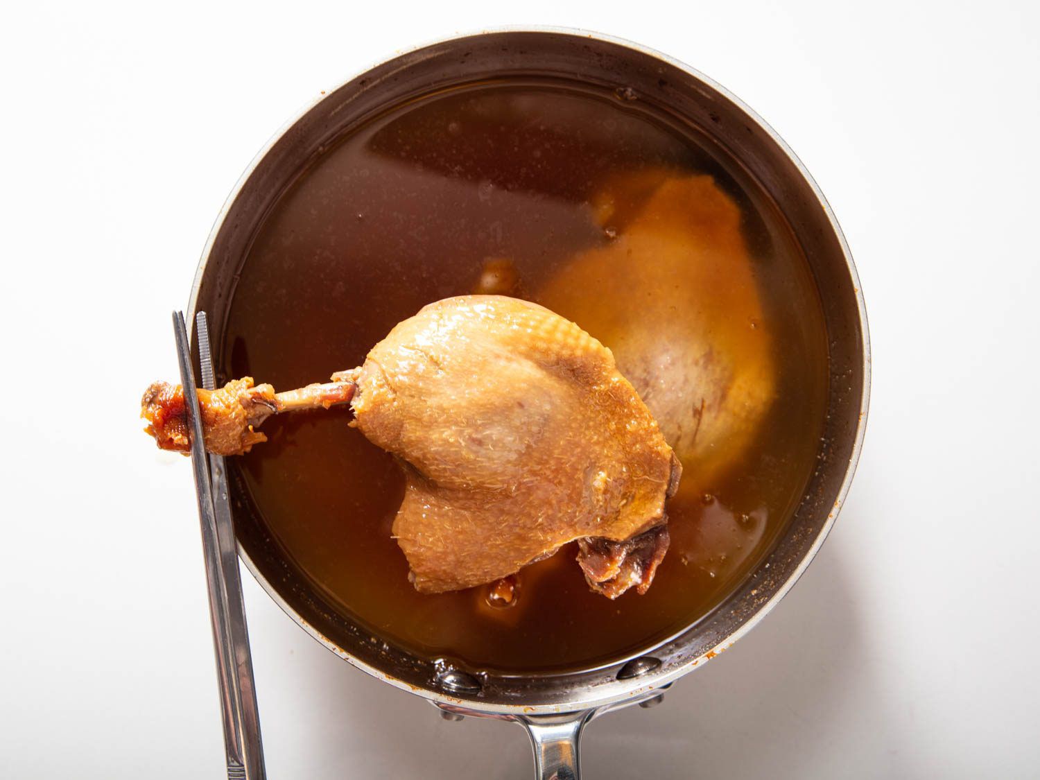 Pulling a leg of koji duck confit out of a saucepan of duck fat.