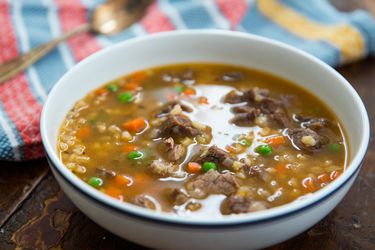 A bowl of pressure cooker beef and barley soup on a table with a striped linen napkin and spoon in the background.