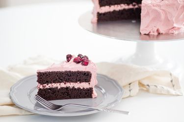 A slice of chocolate cherry layer cake is served on a grey plate. The rest of the cake is visible in the background.