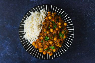 Channa masala and white rice on a blue plate decorated with white lines. The plate is on a dark blue surface.