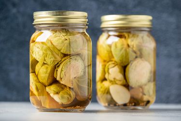 Two glass jars holding pickled brussels sprouts.